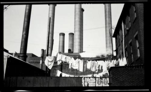 Photograph of laundry hanging in front of smokestacks.