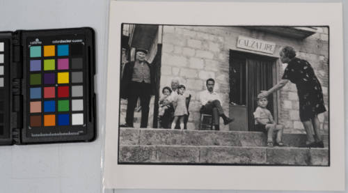 Street scene with grandmother checking grandson’s temperature as family sits outside of shoe store, Sicily