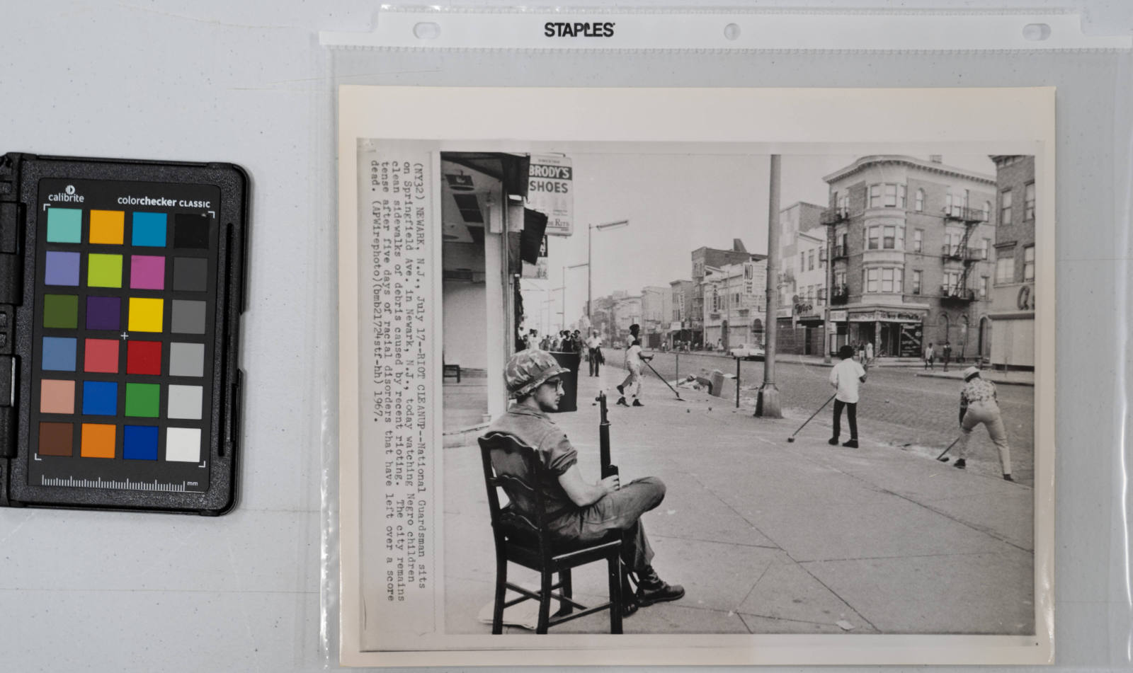 Riot Cleanup: National Guardsman sits on Springfield Avenue in Newark today watching Negro children cleaning sidewalks of debris caused by recent rioting. The city remains tense after five days of racial disorders that have left over a score dead, July 17, 1967