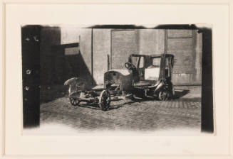 Untitled (Chassis of car, standing before garage door)