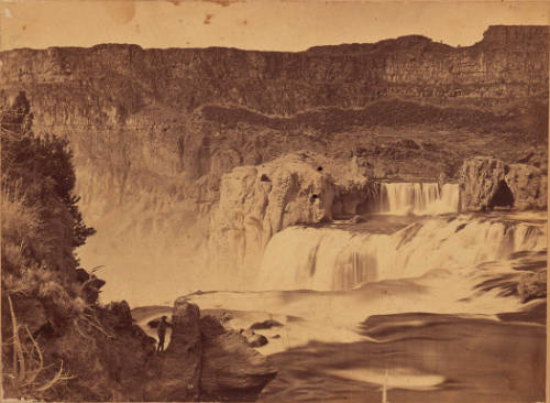 Photographic view across the top of the same waterfall, showing an man standing at the lower left.